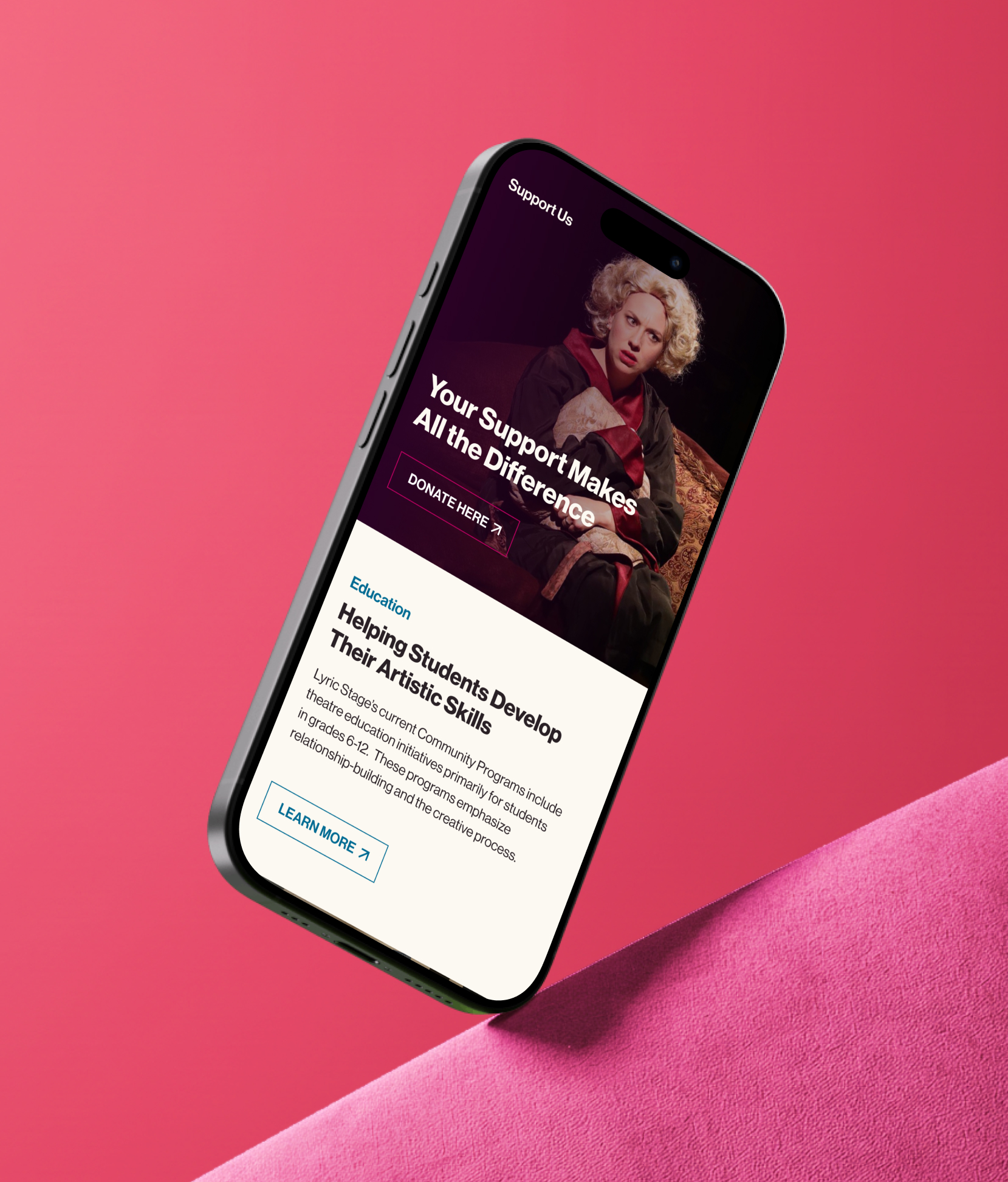 Angled smartphone mockup on a pink background displaying a theater website’s “Support Us” page. The screen features a banner image of a performer and the headline “Your Support Makes All the Difference” with a “Donate Here” button. Below, an education section titled “Helping Students Develop Their Artistic Skills” includes descriptive text and a “Learn More” button.